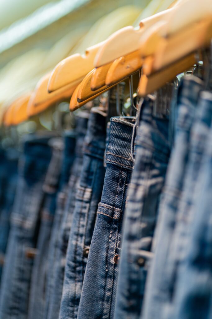 A close-up image of denim jeans neatly arranged on wooden hangers in a store display.